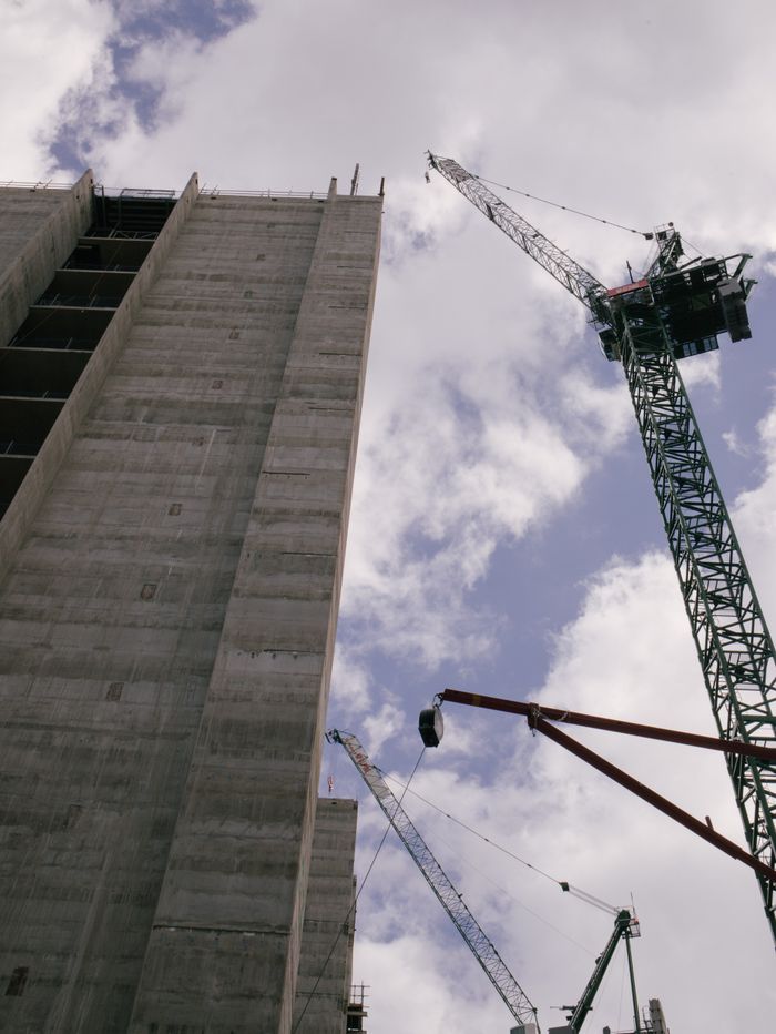 Low angle view of skyscraper under construction with cranes against blue sky.
